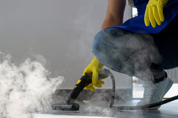 A person in a blue shirt and yellow gloves diligently cleaning a floor with meticulous attention.