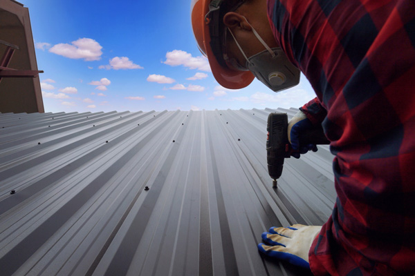 A man in a hard hat and safety glasses working on a metal roof.